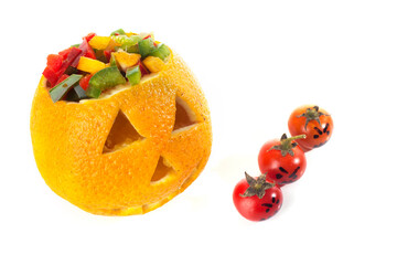 Food art creative concept. Halloween funny faces carved into yellow orange fruit with brain of capsicum vegetables and candies isolated over a white background