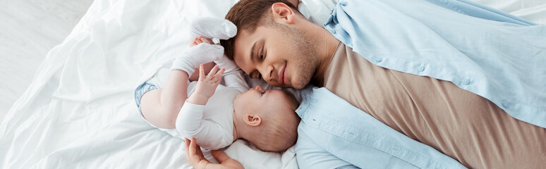 top view of happy father lying on bed face to face with cute baby boy, panoramic shot