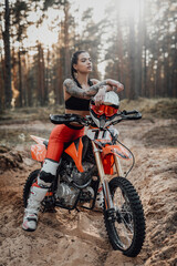 Beautiful female racer wearing motocross outfit with semi naked torso sitting on her bike in the...