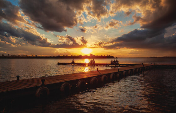 Silhouette of people watching the sunset from the wood pier in Ermida Dom Bosco, Bras&iacute;lia, Distrito Federal, Brazil. Dramatic sunset at Lago Parano&aacute;.