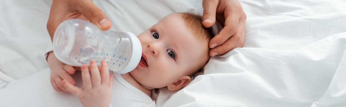 cropped view of father feeding adorable baby boy from baby bottle, horizontal image