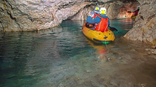 Two young Caucasian boys paddle in underground rocky tunnel on yellow kayak, Podzemlje Pece, Mezica, Slovenia, close up slow motion pan
