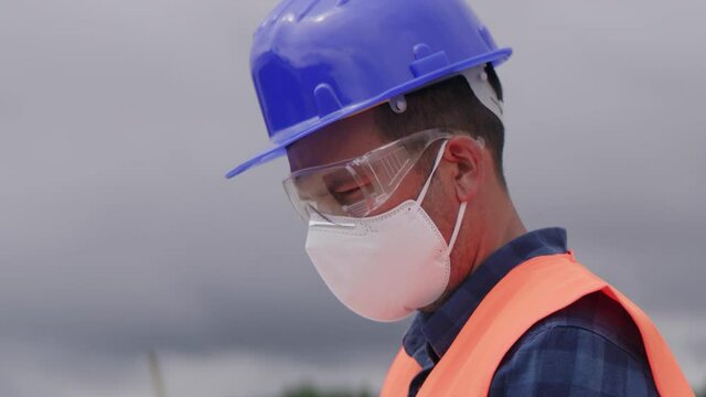 Construction engineer or an architect with a halmet and protective mask on a construction site using a tablet or a laptop.