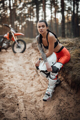 Beautiful brunette girl wearing motocross outfit with semi naked torso sitting on a grass in the...