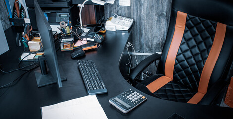 Workplace at table in office with computer, calculator, telephone, cash register. Mouse, keyboard, monitor and large leather chair. Personal space in room for work.  Banner for web site