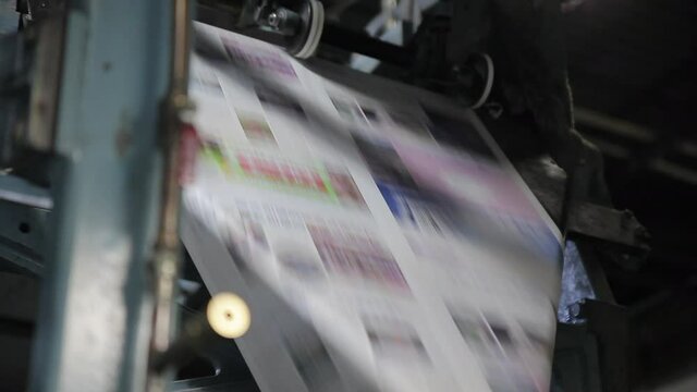 Paper speeds through printing press to produce Chinese language newspaper. View into industrial printing press in operation. Commercial print shop and large scale production operation.