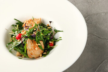 salad with chicken arugula and pine nuts closeup in white plate on grey concrete background