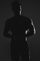Obraz na płótnie Canvas Silhouette of a muscular athlete posing on a dark background