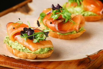 bruschetta with salmon closeup. tapas with salmon on guacamole and topped microgreen on wooden board and black background
