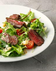 steak salad. Grilled Steak with Mixed Greed Salad cherry tomatoes and parmesan with fresh sauce in white plate on concrete background
