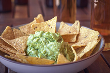 Bowl with guacamole and nachos on a wooden table