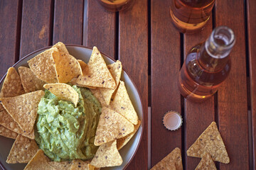Beers and a bowl of guacamole with nachos on an old wooden table, international beer day