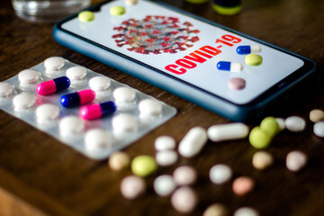 Obraz na płótnie Canvas In this photo illustration pharmaceutical pills are seen displayed on a table with a COVID-19 inscription on the mobile screen. Dexamethasone, Hydroxychloroquine are used to treat coronavirus disease.