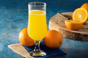 Photograph of glass with orange juice and oranges in  blue background