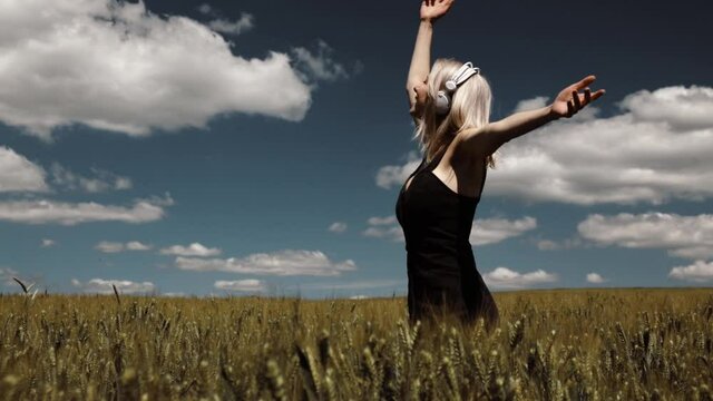 Blonde woman in headphones dancing in wheat field in summer time