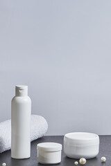 white cosmetic jars for the bath a long tube of pearl towel on a gray background. copy space. mockup. vertical orientation