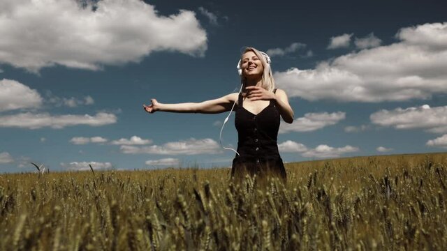 Blonde woman in headphones dancing in wheat field in summer time