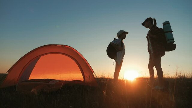 Modern tourist family camping in mountains at sunset. Silhouette mother and daughter resting in a tent camp. Tourism and traveling concept.