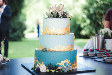 Beautiful three tiered wedding cake. Light blue cake decorated with golden plate and various...