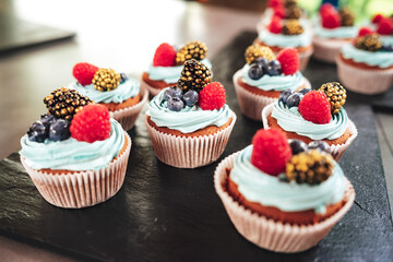 Sweet cupcakes with forest berries on black serving tray. Desserts at party. Celebration, party, birthday or wedding concept.