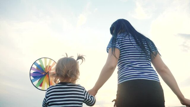 people in the park. happy family together mom and daughter are walking with play pinwheel a wind toy. happy family concept lifestyle. child and mother plays with windmill. girl kid blonde and parent