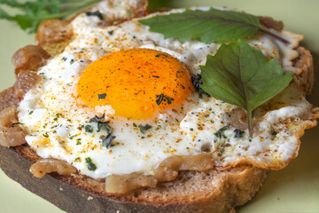 fried eggs with bacon and spices and basil leaves on a slice of brown bread
