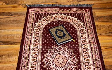 Holy Quran with Arabic calligraphy meaning of Al Quran and prayer mat