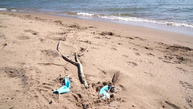 Medical face masks used and thrown on the sand of an empty beach. Covid coronavirus contamination in thea sea.