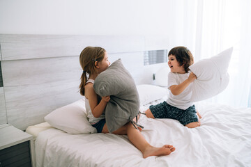 Children playing fight in bed with cushions