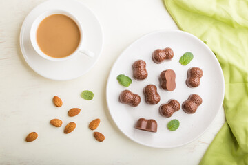 Chocolate candies with almonds and a cup of coffee on a white wooden background. top view.