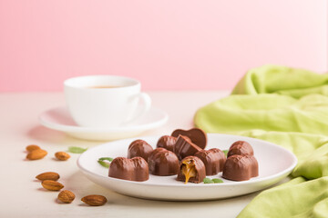 Chocolate caramel candies with almonds and a cup of coffee on a white and pink background. side view, copy space