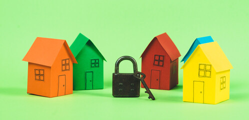 Colored houses on a green background with a closed padlock and a key. Quarantine concept and lockdown.