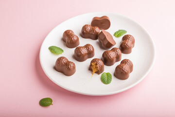 Chocolate caramel candies on a pastel pink background. Side view.
