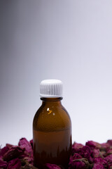 little liquid bottle with no label near a pile of little pink roses. body care and beauty concept. Copy space. High quality photo