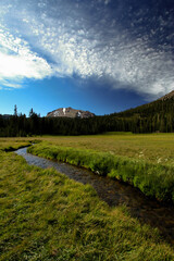 rural meadow with stream and mountain and blue sky
