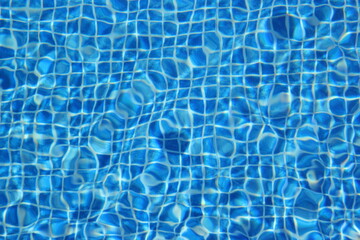 Top view of clear water in a blue tile pool background. Ripple effect
