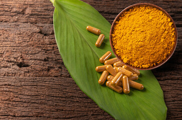 Turmeric powder  in wooden bowl  and capsule on old table. Top view
