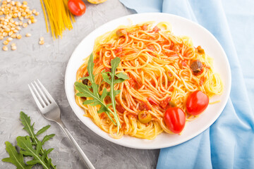 Corn noodles with tomato sauce and arugula on a gray concrete background. Side view, selective focus.