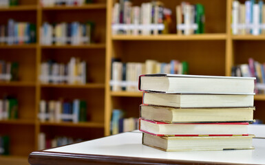 Stack of books on wood table and blurred bookshelf in the library, education background, back to school concept.