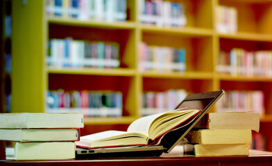 Stack of books with laptop on table in library, image selective focus and blurred bookshelf in the library, education background, back to school concept.