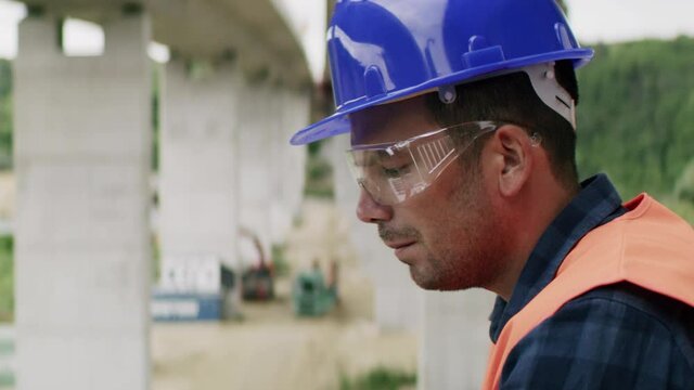 Construction engineer or an architect with a halmet and protective equipment on a building construction site using a laptop.