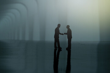 Fototapeta na wymiar Silhouette of two businessmen make an handshake partnership agreement. Miniature people figure conceptual photography