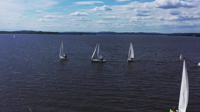 Several beautiful white yachts sailing across the beautiful pond. Video. Aerial view of small sailing boats on the river during competition on blue cloudy sky background.