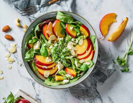 Fresh summer salad with peach, spinach, micro greens, feta cheese and almonds on light marble background. Healthy food, clean eating, Buddha bowl salad, top view
