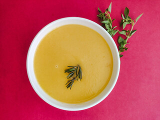 Bowl of yellow soup in red background and basil