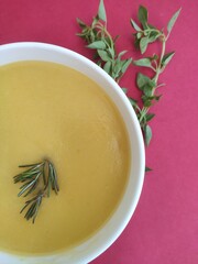 Bowl of yellow vegetable soup with basil on red background 