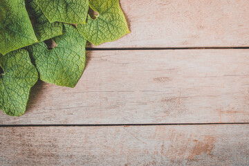Green leaves on a wooden table background, free space, top view.