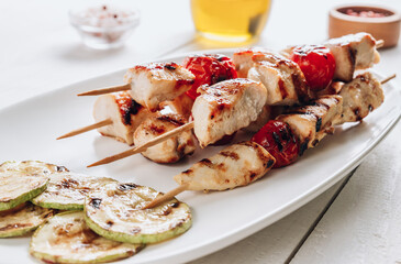 Grilled chicken skewers with cherry tomatoes on plate. White wooden table.