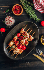 Grilled chicken skewers with cherry tomatoes on plate. Black wooden table.