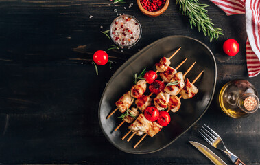 Grilled chicken skewers with cherry tomatoes on plate. Black wooden table.